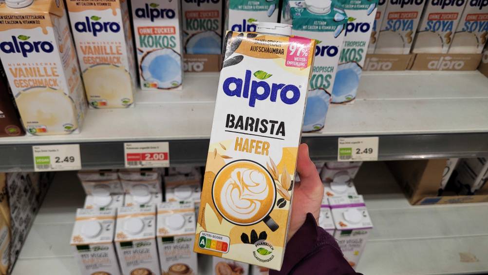 Eine Hand hält eine Packung des Barista-Haferdrink im Test vor ein Regal.