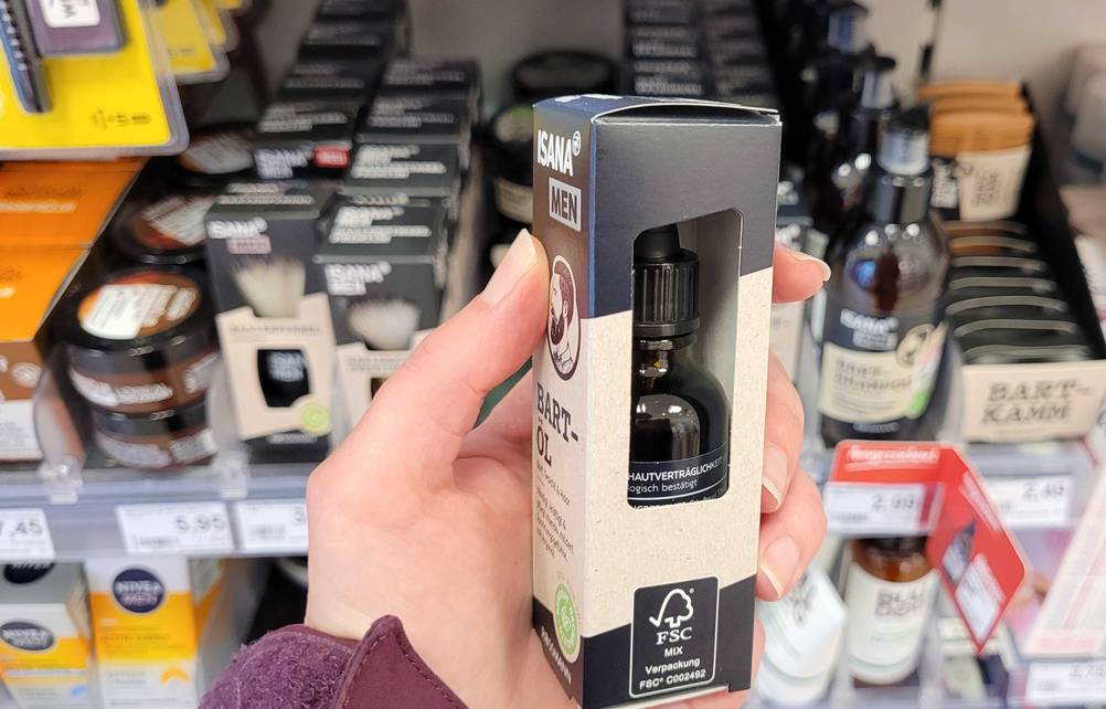 Im Test: Eine Hand hält eine Flasche Bartöl in der Originalverpackung vor ein Verkaufsregal.
