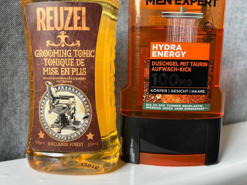 Nahaufnahme der Labels zweier getesteter Bartshampoos vor einer grauen Fläche.