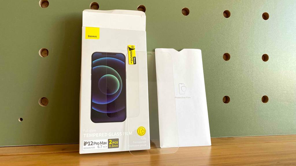 Im Test: Ein mit Schutz versehenes Iphone-12-Pro-Max-Panzerglas und die geöffnete Verpackung dazu lehnen nebeneinander an einer Lochwand.
