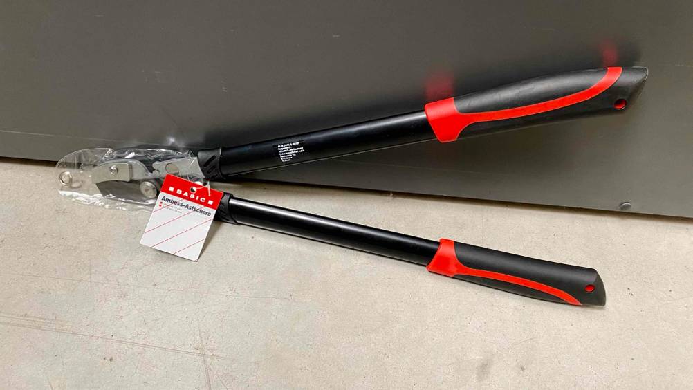 Eine getestete Amboss-Astschere verpackt mit Label lehnt an einer Metallwand auf einem hellen Boden