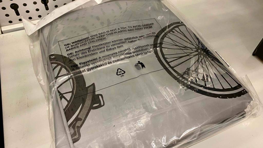 Fahrradschutzhüllen-Test: Nahaufnahme einer grauen, mit schwarzen Zweirädern bedruckten Schutzhülle, die sich gefaltet in einer transparenten Plastikverpackung befindet.