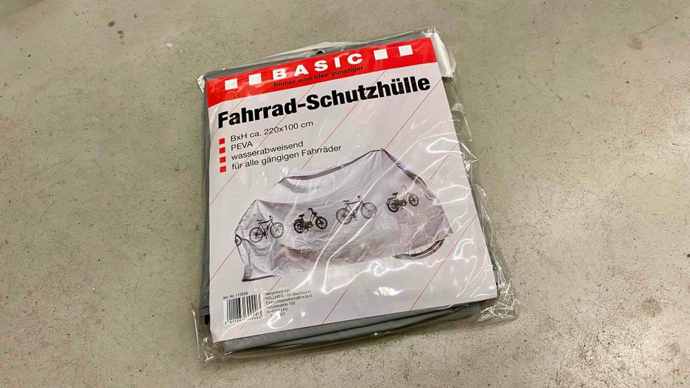 Eine getestete Fahrradschutzhülle in ihrer Originalverpackung von vorne auf einem Betonboden.