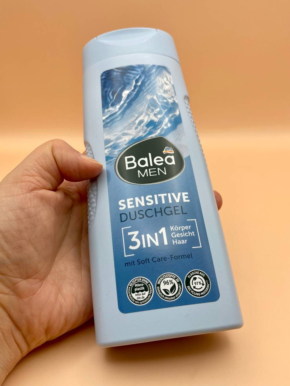 Eine Hand hält eine Flasche des getesteten basischen Duschgels vor eine gelbe Fläche.