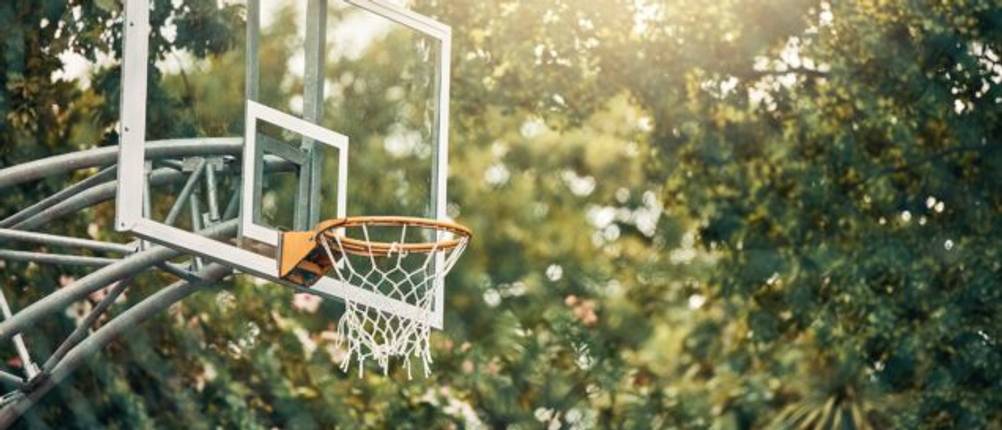 Getestete Basketballanlage vor einem Hintergrund aus Bäumen und Sonnenlicht.