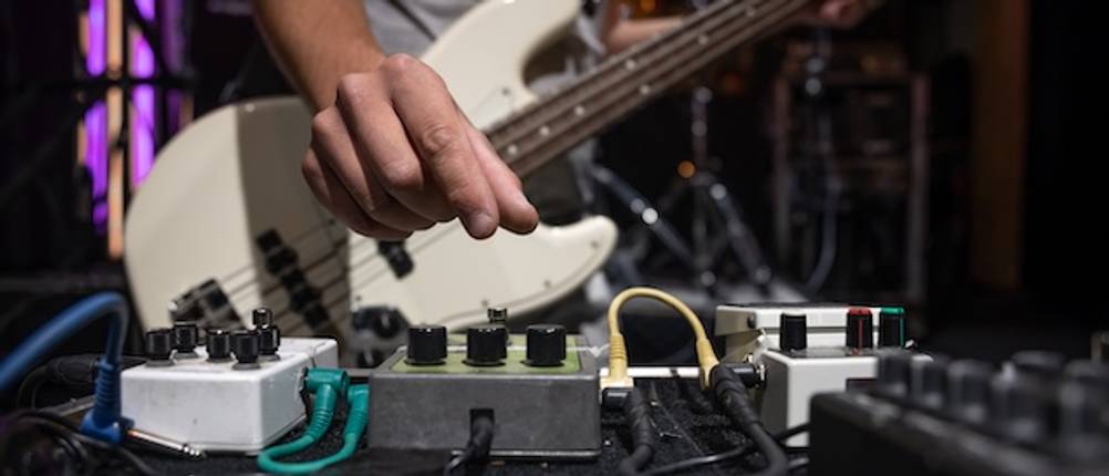 Nahaufnahme einer Hand eines Mannes der einen Bass testet und Effekte für den Bass einstellt.