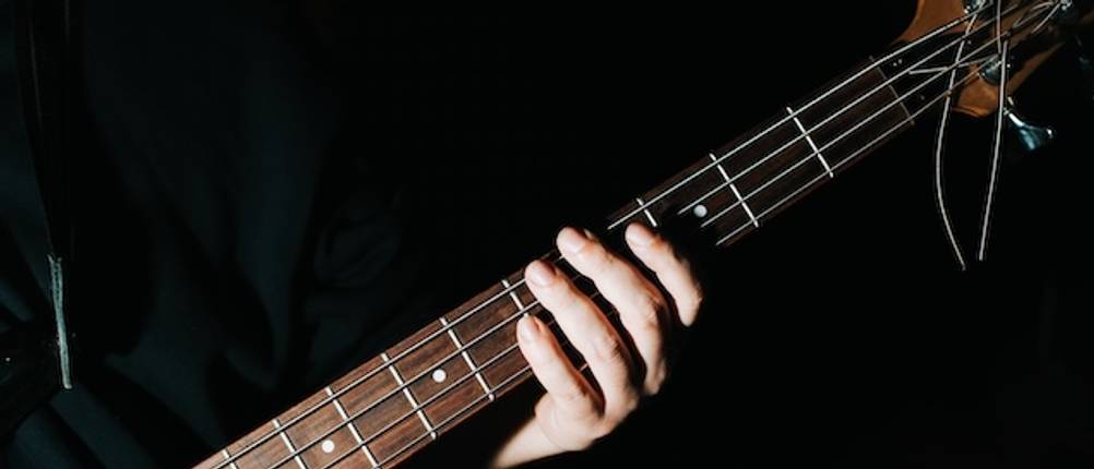 Bass-Test: Eine männliche Hand greift auf dem Griffbretts eines E-Basses vor einem dunklen Hintergrund.