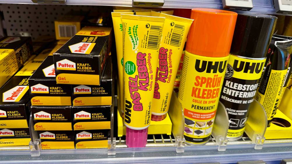 Mehrere Tuben des getesteten Bastelklebers in einem Verkaufsregal neben anderen Produkten.