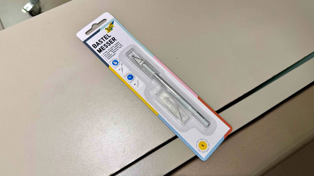 Ein getestetes Bastelmesser in Originalverpackung auf einer hellen Fläche.