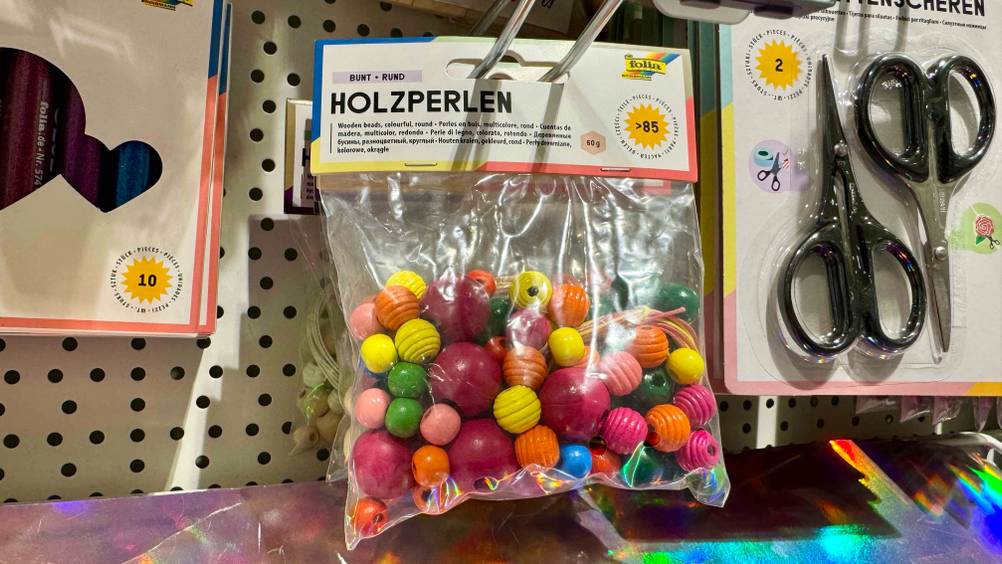 In einem Regal hängen mehrere Packungen der gestesteten Bastelperlen neben anderen Produkten.