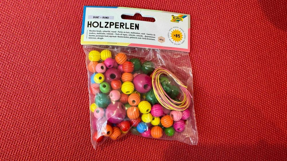Getestet: Eine Packung Bastelperlen auf einem roten Polster.