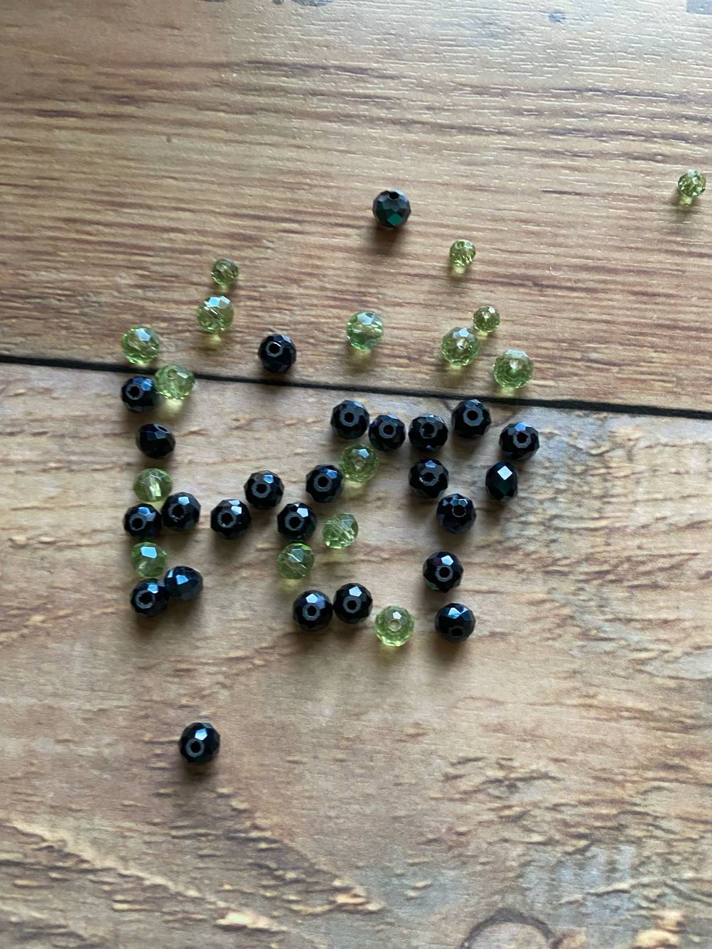 Auf einer Holzfläche liegen die getesteten Bastelperlen in schwarz und grün.