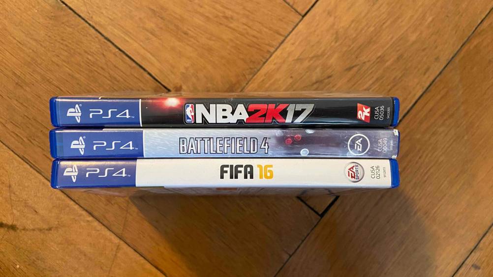 PS5-Spiele im Test: Drei übereinandergestapelte PS4-Spiele im Test befinden sich auf einem Holzboden.