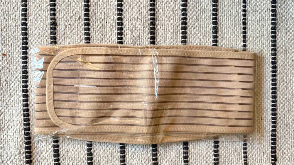 Ein Bauchgurt Schwangerschaft im Test in seiner transparenten Verpackung auf einem Teppich.