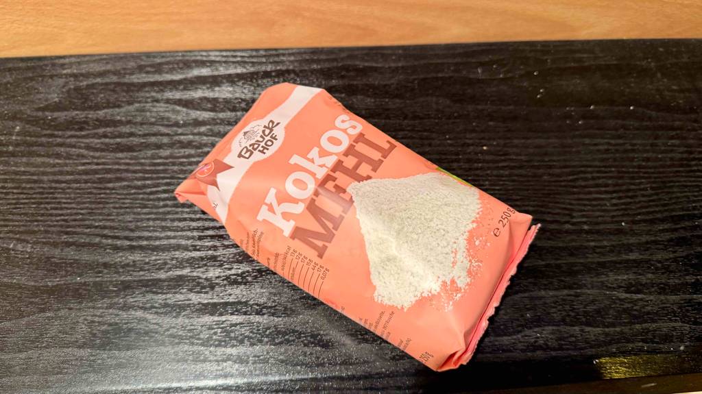 Eine 250-g-Packung Kokosmehl im Test liegt auf einer schwarzen Holzfläche.