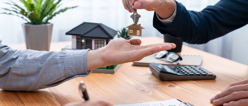 Baufinanzierung-Test: Ein Mann unterschreibt einen Kreditvertrag und der Berater übergibt ihm einen Hausschlüssel.