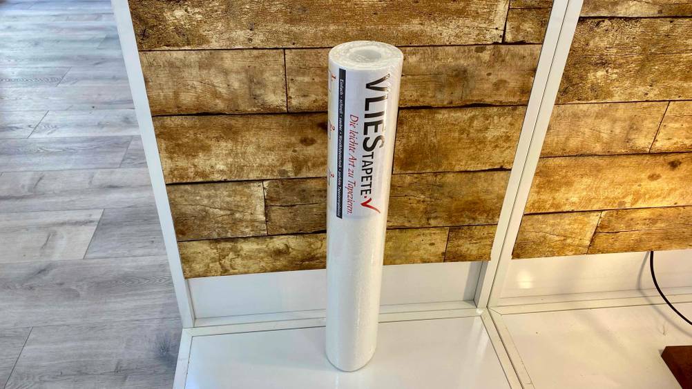 Im Test: Eine Rolle Vliestapete steht auf einem Sockel vor einer Holzwand.