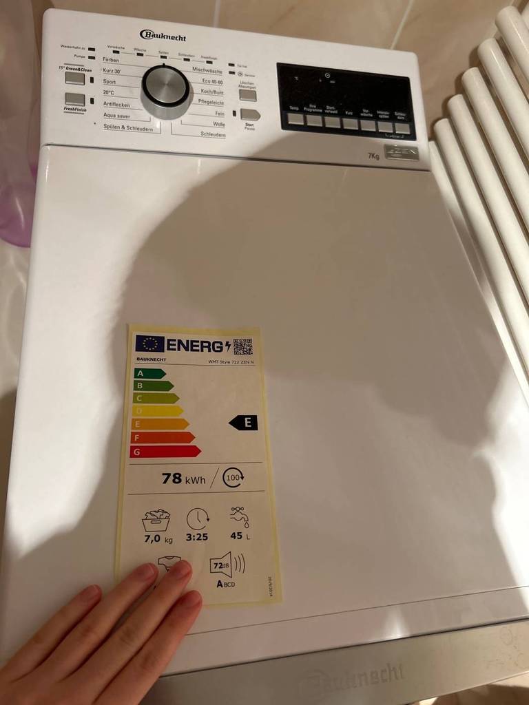 Ansicht von oben auf eine getestete Bauknecht-Toplader-Waschmaschine im häuslichen Bereich mit Fokus auf das Energielabel.