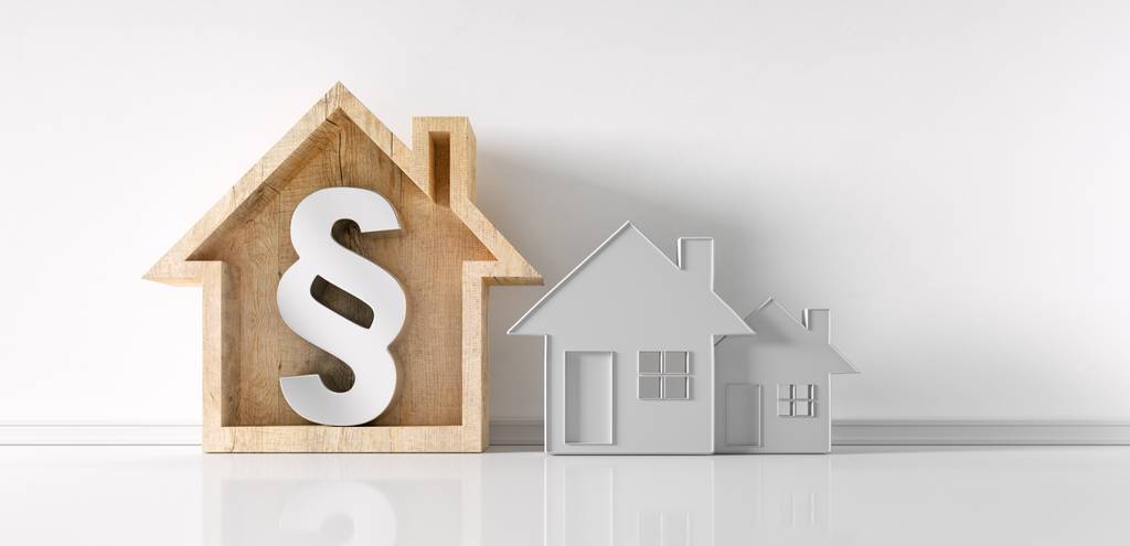 Drei Häuser als Modelle stehen in einer Illustration nebeneinander. Das erste ist aus Holz und hat ein großes Paragraphen-Symbol integriert.