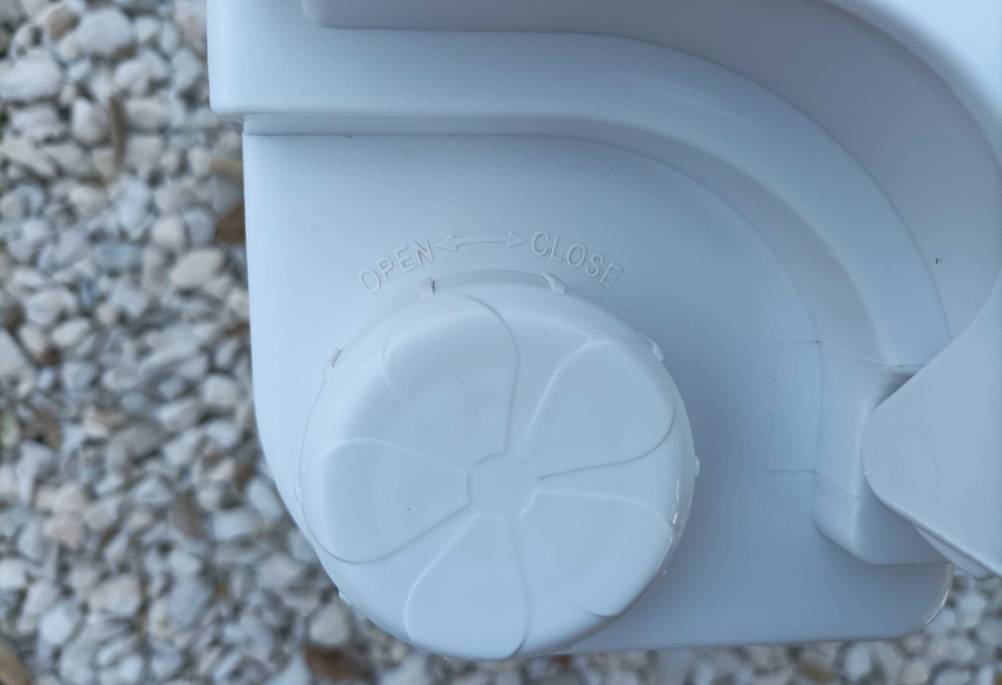 Detailansicht des Drehverschlusses einer weißen Campingtoilette im Test auf Schotter.