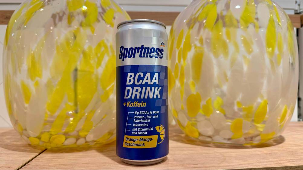 Getestet: Ein BCAA-Drink vor zwei gelb-weißen Vasen auf einem Holzbrett.