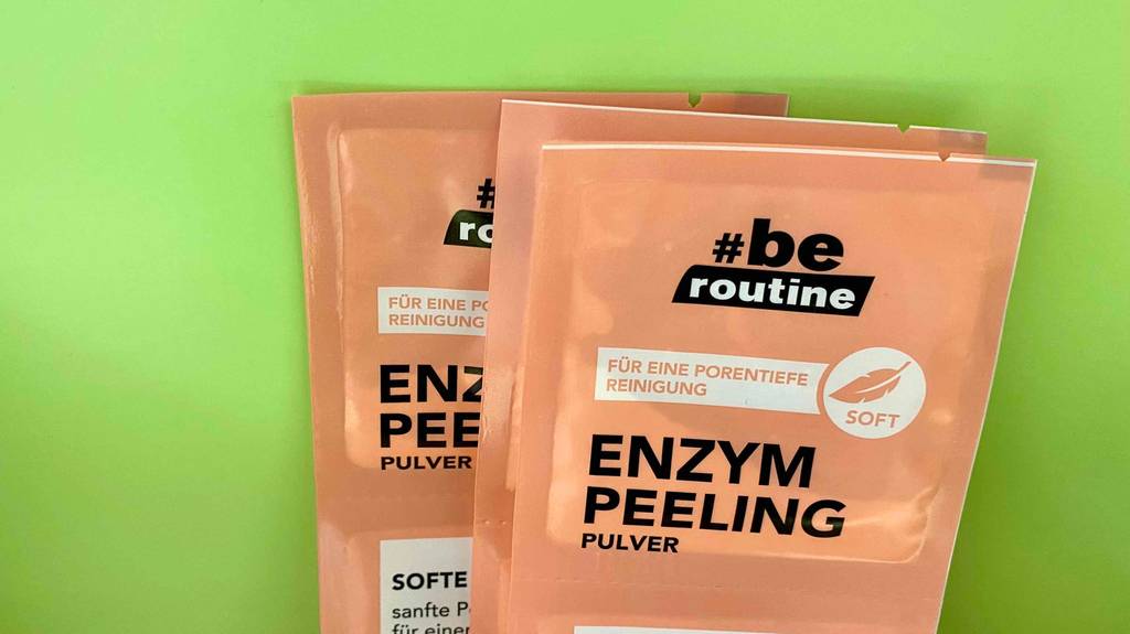 drei übereinanderliegende Packungen Enzympeeling von be routine liegen auf einem grünen Untergrund.