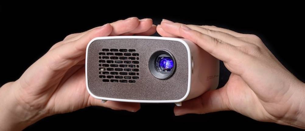 Beamer unter 100 Euro im Test: Ein Mini-Beamer wird in zwei Händen vor schwarzem Hintergrund gehalten.