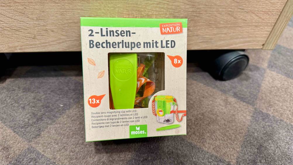 Auf dem Boden vor einem Rollcontainer steht die Becherlupe im Test.