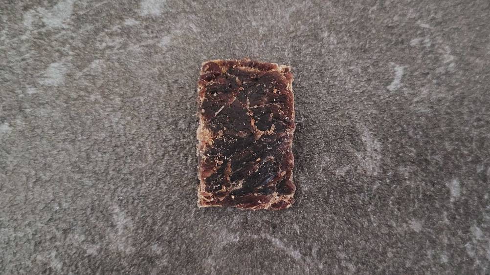 Nahaufnahme eines einzelnen Beef Jerkys im Test auf einer grauen Fläche.