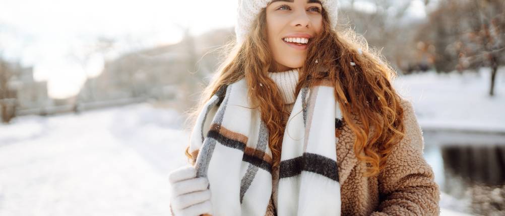 Beheizbare Jacken für Damen im Test: Frau in einer Winterlandschaft, bekleidet mit Mütze, Schal, Handschuhe und Winterjacke