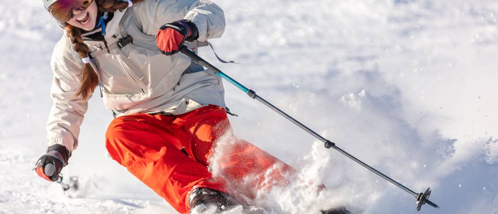 Beheizbare Jacken für Damen im Test: Frau, die auf Skiern die Piste hinunterfährt und dabei großen Spaß hat