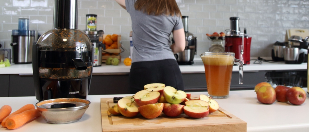 Auf einem Holzbrett liegen einige halbierte Äpfel, daneben steht ein Entsafter.