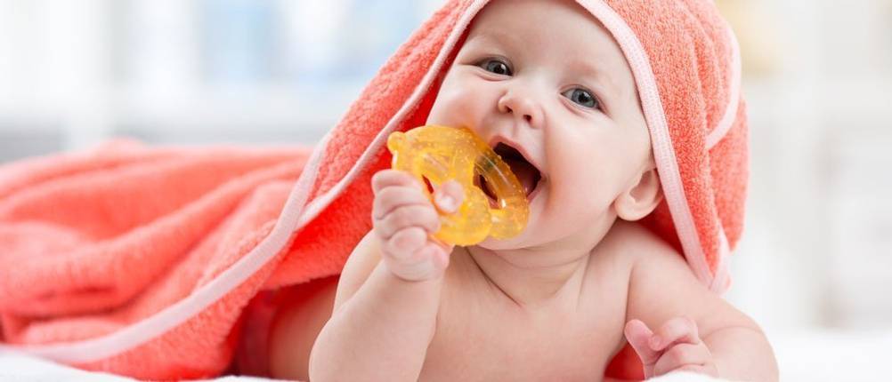 Beißring-Test: fröhliches Baby beißt auf gelben Beißring