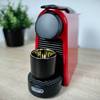 Die Nespresso De’Longhi Essenza Mini in Rot steht auf einer Arbeitsfläche. Eine schwarze Tasse ist unter dem Kaffeeauslauf positioniert.