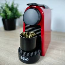 Die Nespresso De’Longhi Essenza Mini in Rot steht auf einer Arbeitsfläche. Eine schwarze Tasse ist unter dem Kaffeeauslauf positioniert.