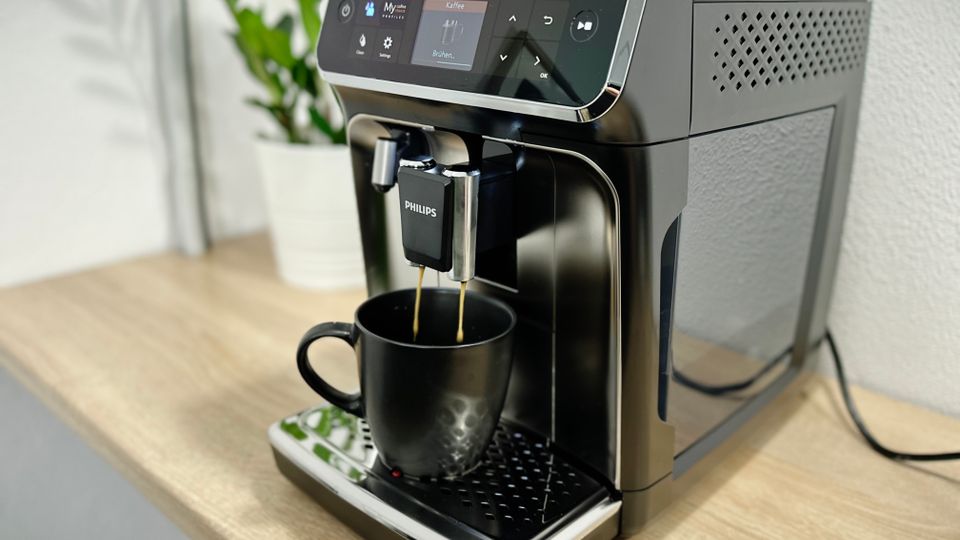 Der Philips Series 5400 (EP5447/90) Kaffeevollautomat bereitet gerade frischen Kaffee zu. Der Auslauf füllt eine schwarze Tasse auf der Abtropffläche.
