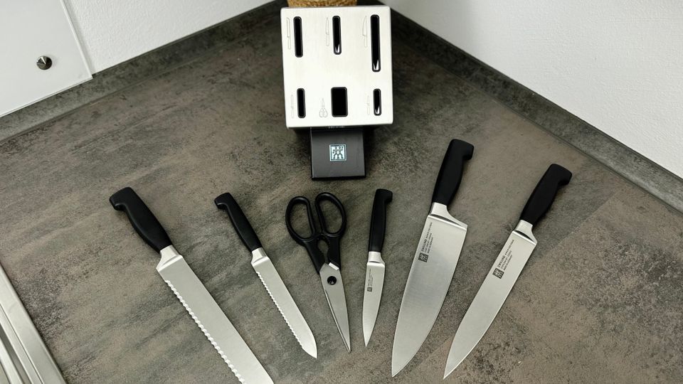 Mehrere Messer liegen ausgebreitet auf einer Küchenarbeitsfläche. Im Hintergrund sieht man einen Messerblock von oben.