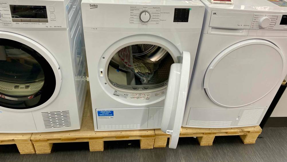 Beko-Trockner getestet: Ein Gerät mit geöffneter Klappe von vorne zwischen anderen Geräten.