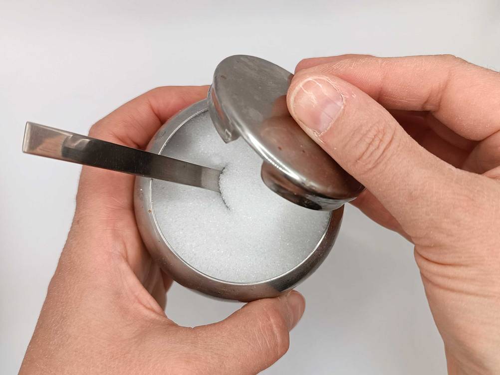 Im Test: Eine Hand hält eine Dose Zucker mit Löffel.