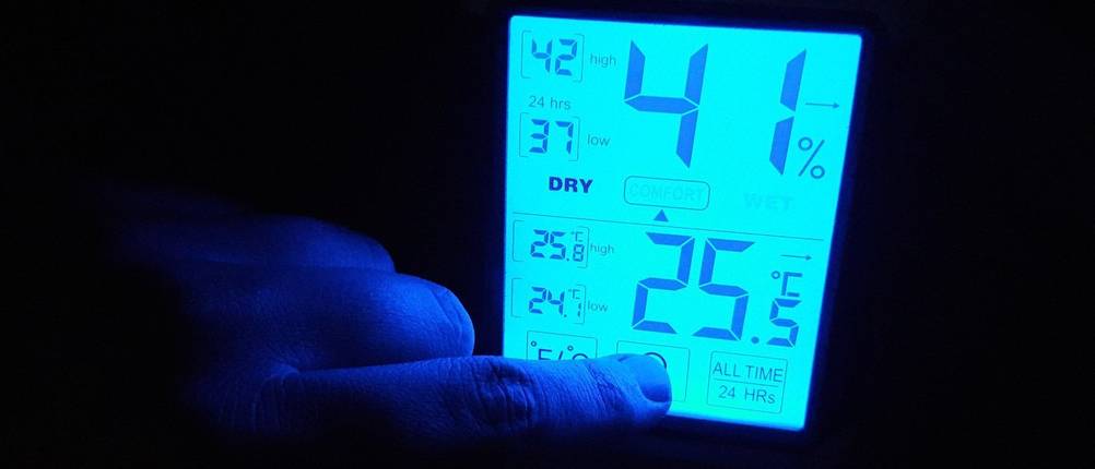 Ein Finger drückt den Beleuchtungs-Knopf eines Hygrometer-Displays