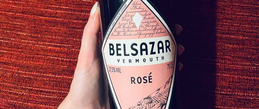 Hand hält einen 17,5-prozentigen Belsazar Rosé Vermouth im Test vor rotem Hintergrund.