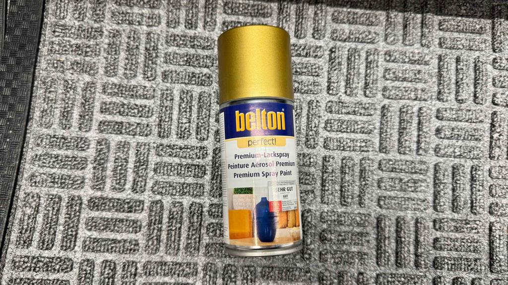 Goldspray im Test: Eine Spraydose liegt auf einer grauen Fußmatte.