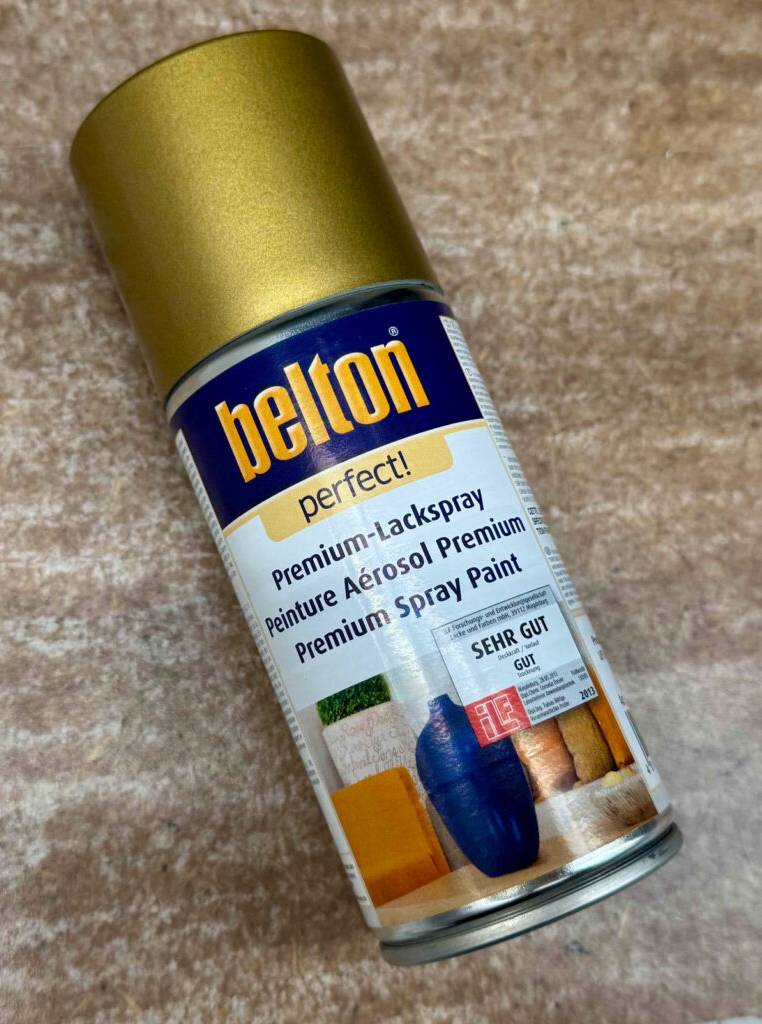 Die Spraydose mit dem getesteten Goldspray liegt auf einem beigefarbenen Teppich.