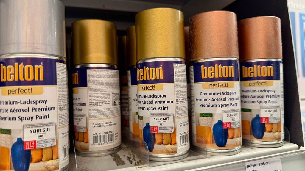 Mehrere Dosen mit Goldspray im Test stehen nebeneinander auf einem Verkaufsregal.