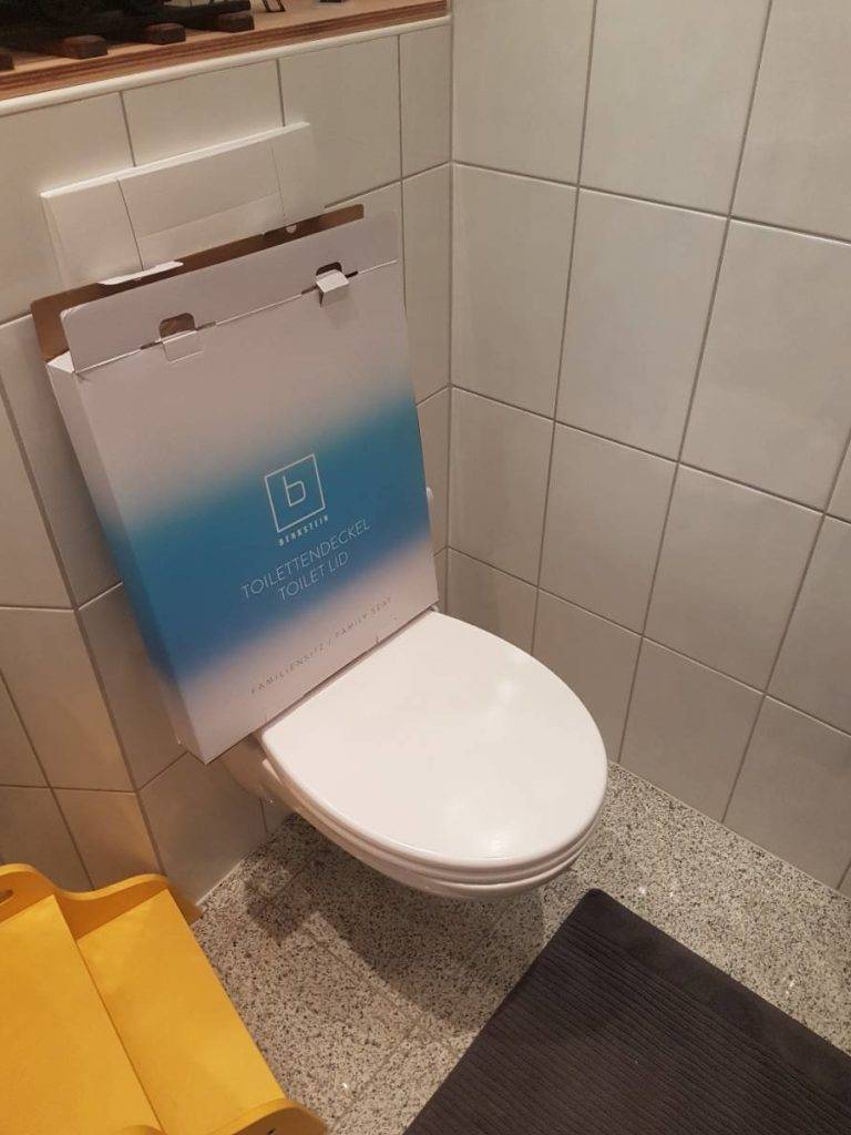 WC-Sitz mit Absenkautomatik im Test: Originalverpackung eines Benkstein Toilettendeckels steht auf einem geschlossenen weißen Deckel auf einer Toilette.