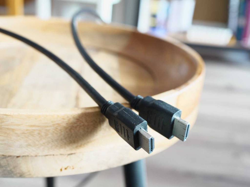 Detailansicht zweier Anschlüsse von einem schwarzen, getesteten HDMI-2.1-Kabel auf einem Holzteller.
