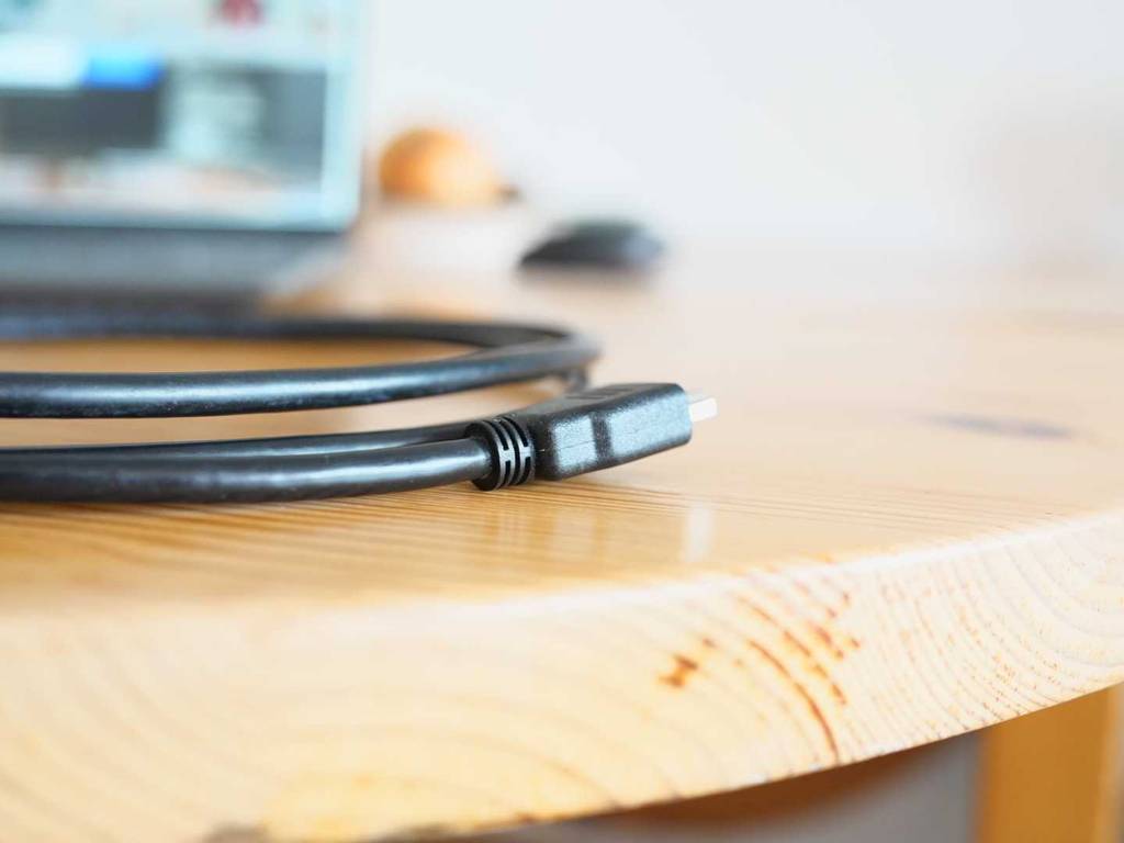Ein getestetes HDMI-2.1-Kabel liegt auf einem Holztisch, im Hintergrund steht ein eingeschalteter Laptop.