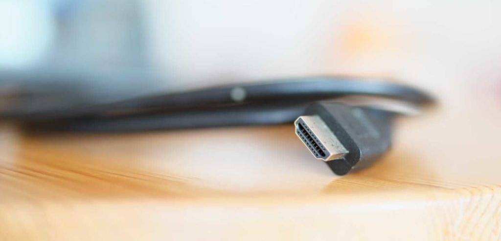 HDMI-2.1-Kabel-Test: Nahaufnahme des silbernen Anschlusses eines schwarzen Kabels auf einer Holzfläche.