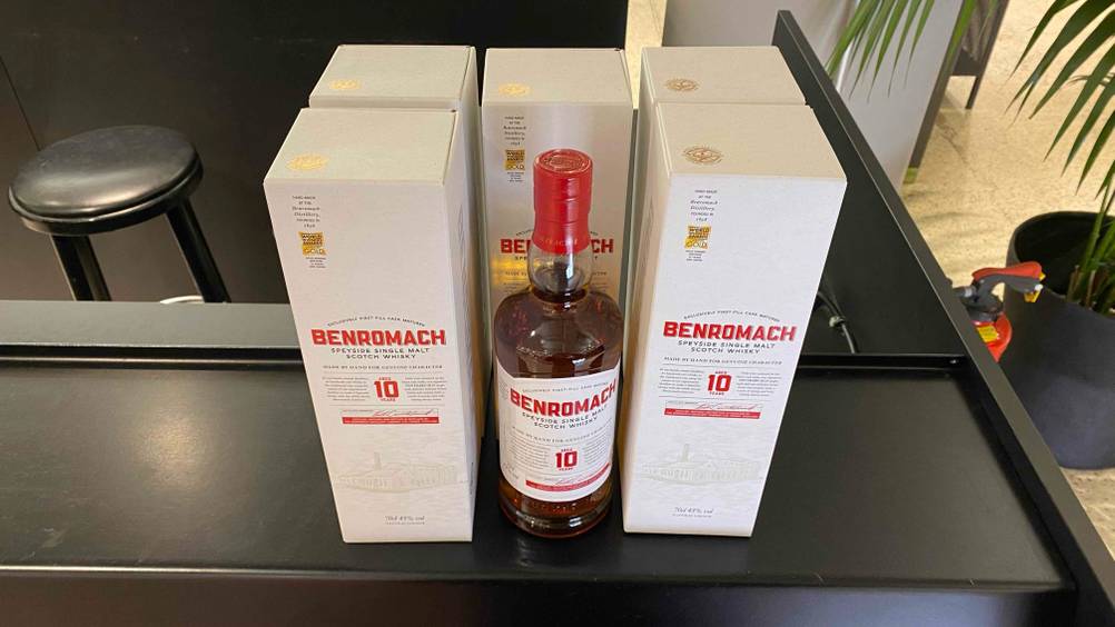 Im Test: Zwischen fünf im Kreis angeordneten Originalverpackungen steht eine Flasche Single-Malt-Scotch-Whisky auf einer dunklen Fläche.