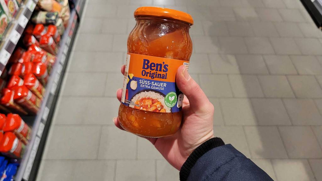 Eine Hand hält ein Glas Süß-Sauer-Sosse zum testen.